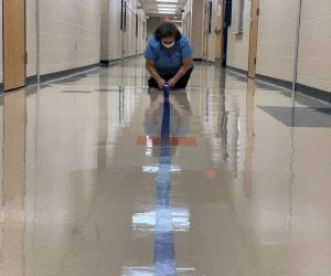 Campus custodian laying tape on the floor for social distancing.
