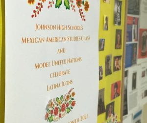 A brightly colored poster board is decorated with red and orange flowers. The poster reads "Johnson High School's Mexican American Studies Class and Model United Nations Celebrate Latina Icons, Hispanic Heritage Month 2021." The poster is surrounded by bright photos of various Latina Icons in Mexican American history.