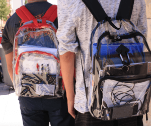 Two students walking outdoors with their clear backpacks.
