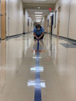 Campus custodian laying tape on the floor for social distancing.