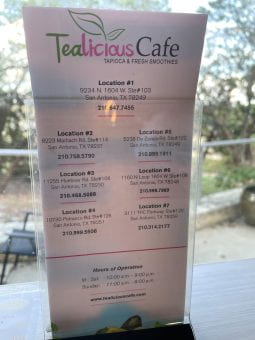 The locations of Tealicious cafe are listed on a card standing on a counter by a window.