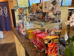 The snack bar boasts soft mochi boxes, shrimp crackers, pocky, and other treats. The glass is decorated with cute boba stickers. 
