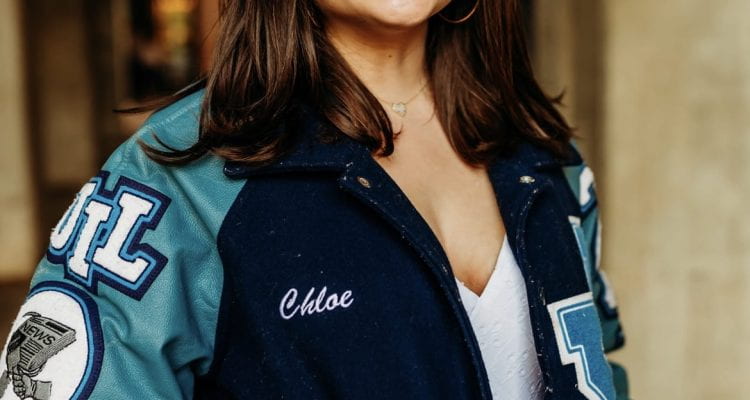 Senior and Editor-In-Chief Chloe Jordan smiles in her blue letterman with journalism patches and a white dress