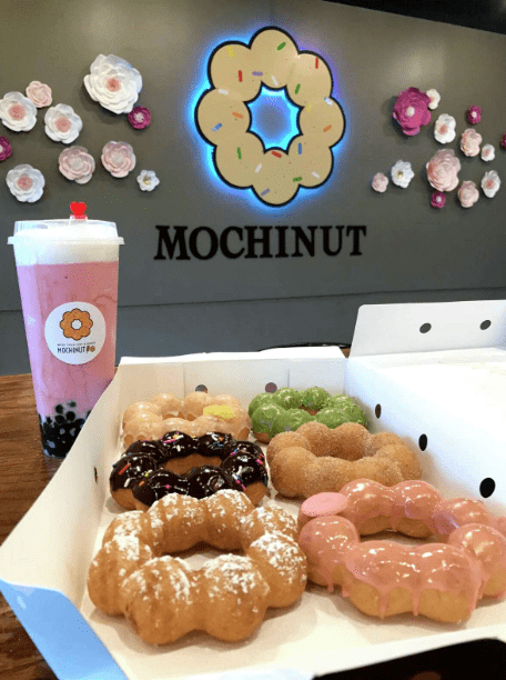 6 mochi donuts of various flavors and pink boba and mochinut decor on the wall