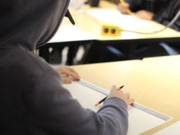 Student wearing black baseball cap and black hoodie while using a ruler.